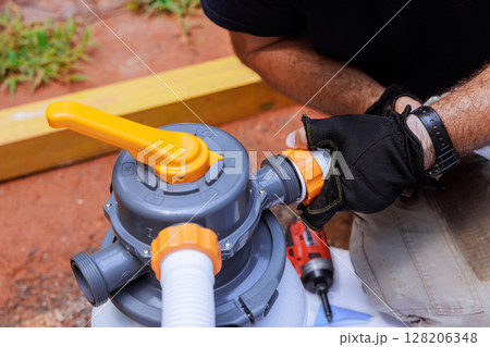 Individual works on connecting parts of pool filter in home backyard, showing tools equipment used. 128206348