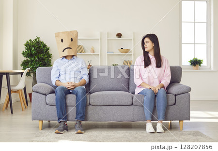 Couple sitting on opposite sides of sofa with upset faces ignoring each other. Couple sitting on opposite sides of sofa with upset faces ignoring each other. 128207856