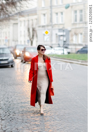Stylish businesswoman walking down cobblestone street in red coat Stylish businesswoman walking down cobblestone street in red coat 128208061