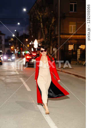 Fashionable woman walking down city street at night 128208066