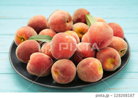 Sweet peaches and leaves on dark plate on blue wooden background. 128208187