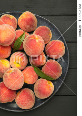 Sweet peaches and leaves on dark plate on black wooden background. Vertical photo 128208188