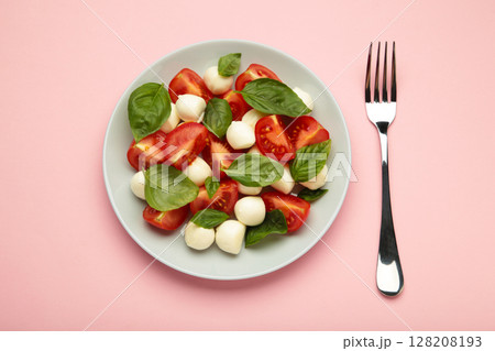 Italian Caprese salad with cherry tomatoes, mozzarella, basil on dark plate on pink background. 128208193