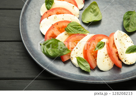Italian Caprese salad with cherry tomatoes, mozzarella, basil on dark plate on black background. Italian Caprese salad with cherry tomatoes, mozzarella, basil on dark plate on black background. 128208213