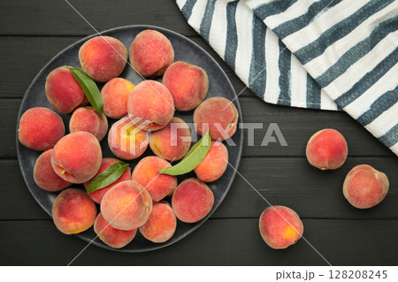 Sweet peaches and leaves on dark plate on black wooden background. 128208245