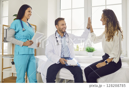 Doctor giving high five with a young happy woman patient in medical clinic. Doctor giving high five with a young happy woman patient in medical clinic. 128208785