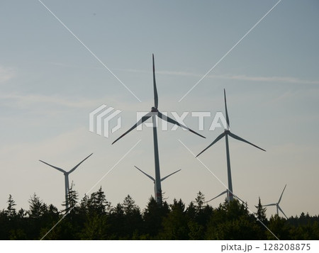 Group of wind turbines are in the sky, with the sun setting behind them 128208875