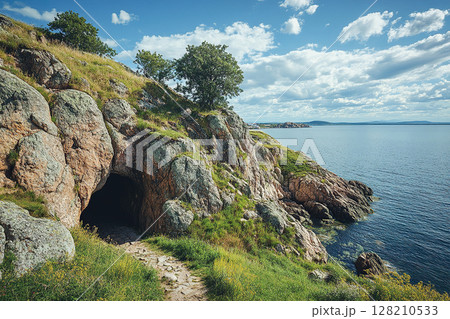 Rocky coastal cliffs with large boulders and a cave entrance overlooking the sea. Generated by artificial intelligence 128210533