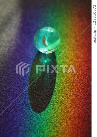 Small, clear, blue ball sits on a colorful surface Small, clear, blue ball sits on a colorful surface 128210572