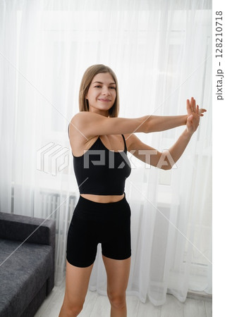 Young woman doing morning stretch in black sportswear at home. Young woman doing morning stretch in black sportswear at home. 128210718