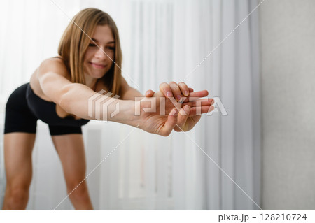 Focus on clasped hands of a young woman stretching forward in black sportswear. 128210724