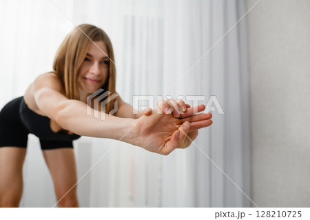 Focus on clasped hands of a young woman stretching forward in black sportswear. Focus on clasped hands of a young woman stretching forward in black sportswear. 128210725