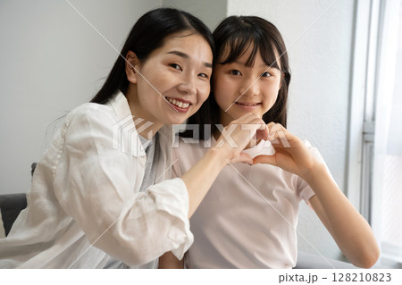 屋内で手でハートマークをつくる母娘 128210823