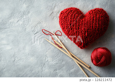 A knitted red heart with knitting needles and a ball of red thread lies on a concrete surface. Knitting. Valentine's Day. A DIY gift. 128211472