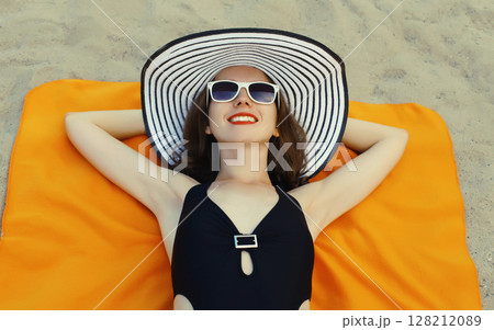 Summer vacation, beautiful happy relaxing young woman in swimsuit lying on sand on the beach 128212089