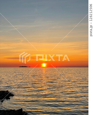 Beautiful sunset over the sea. The sun sets on the water. The sky is painted with bright colors. Sunny path on the water. Summer evening. Sunset beach. Vertical photo. 128212506
