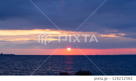 Scenic sunset over the sea. The sun is peeking out from behind the clouds. 128212562