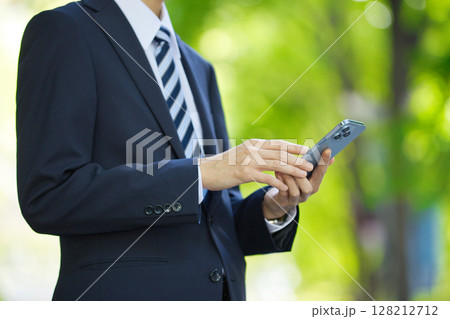 ビジネス街でスマートフォンを見るスーツの若いビジネスマン 128212712