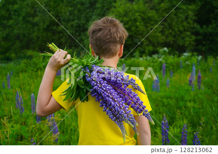 The scene depicts a boy in yellow, radiating happiness in a lush lupine-filled landscape. The scene depicts a boy in yellow, radiating happiness in a lush lupine-filled landscape. 128213062