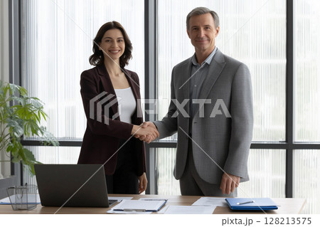 Cheerful Young Manager Welcomes New Employee with a Handshake in Modern Office Setting 128213575