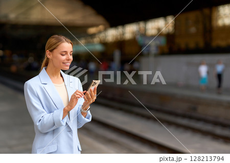 A woman engaged in using her smartphone at a bustling train station while commuting 128213794