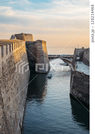General view of the moat of the Royal Walls of Ceuta at sunset while a ship crosses it 128214468