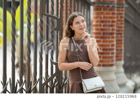 Pretty young woman traveler in summer dress with handbag posing near Hospital de la Santa Creu i Sant Pau in Barcelona on spring day Pretty young woman traveler in summer dress with handbag posing near Hospital de la Santa Creu i Sant Pau in Barcelona on spring day 128215968