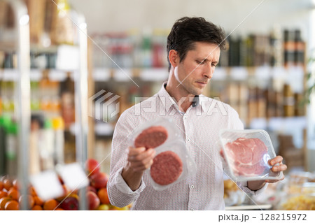Man in light shirt choose and buy raw cooled beef entrecote and hamburger cutlet in store 128215972