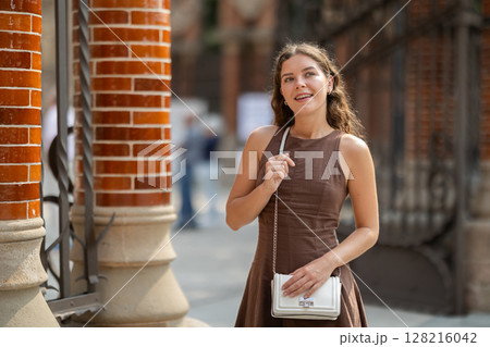 Young woman traveler in summer dress with handbag enjoying walk near columns of architectural complex of Hospital de la Santa Creu i Sant Pau in Barcelona on spring day Young woman traveler in summer dress with handbag enjoying walk near columns of architectural complex of Hospital de la Santa Creu i Sant Pau in Barcelona on spring day 128216042