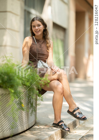 Young woman sitting on a concrete flower bed 128216047