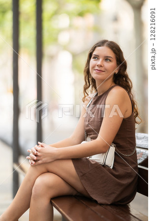 Young woman sitting on a bench in a European city 128216091