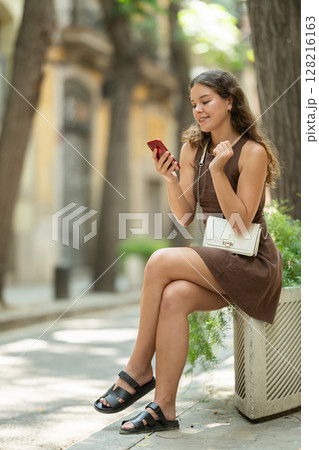 Woman holding mobile phone in her hands and sitting in a flower bed Woman holding mobile phone in her hands and sitting in a flower bed 128216163