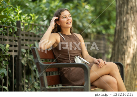 Young woman sitting on a bench in a European city 128216215