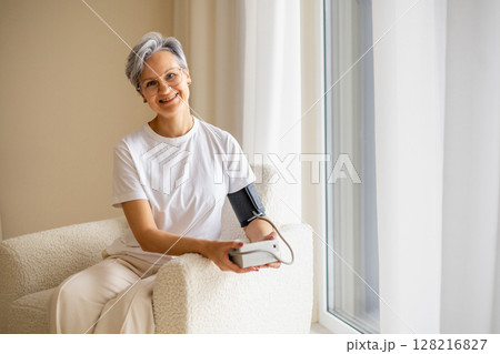 A mature elderly, well-groomed, beautiful woman pensioner with gray hair measures blood pressure A mature elderly, well-groomed, beautiful woman pensioner with gray hair measures blood pressure 128216827