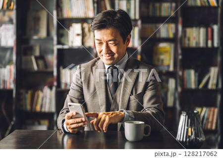 図書館,書斎でスマホを使うアジア人男性ビジネスマン（電子書籍,読書,文学,教養,レトロ） 128217062