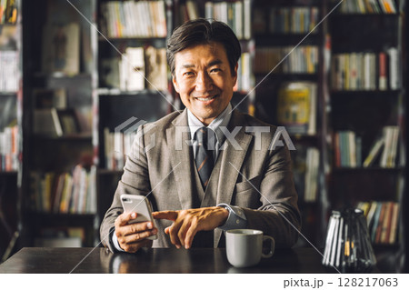 図書館,書斎でスマホを使うアジア人男性ビジネスマン（電子書籍,読書,文学,教養,アプリ） 128217063