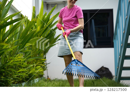 A woman raking the lawn at the backyard of her house A woman raking the lawn at the backyard of her house 128217500