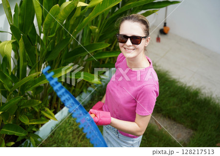 A woman raking the lawn at the backyard of her house  128217513