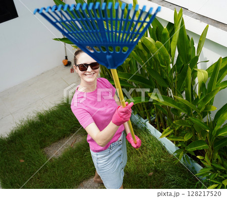 A woman raking the lawn at the backyard of her house  128217520
