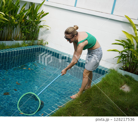 A young woman clean leaves out of a pool  128217536