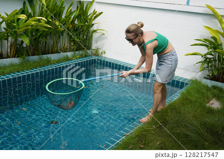 A young woman clean leaves out of a pool A young woman clean leaves out of a pool 128217547