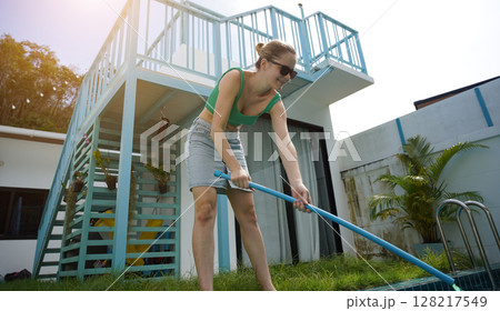 A young woman clean leaves out of a pool A young woman clean leaves out of a pool 128217549