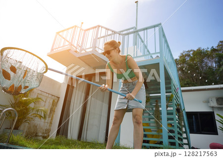 A young woman clean leaves out of a pool A young woman clean leaves out of a pool 128217563