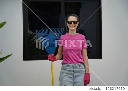 A woman raking the lawn at the backyard of her house  128217610
