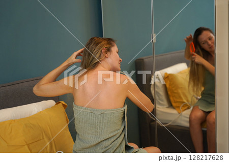 A woman is expertly styling her hair using a blow dryer and brush while in the bathroom 128217628