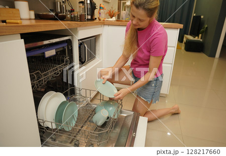 Young woman takes dishes out of the dishwasher machine 128217660