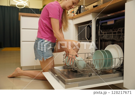 Young woman takes dishes out of the dishwasher machine Young woman takes dishes out of the dishwasher machine 128217671