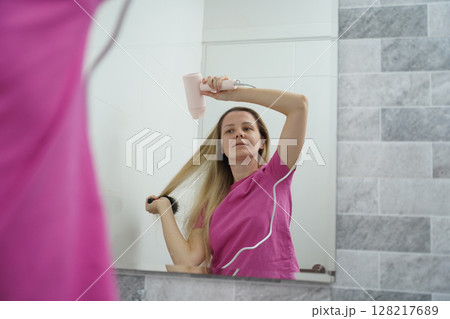 A woman is expertly styling her hair using a blow dryer and brush while in the bathroom 128217689