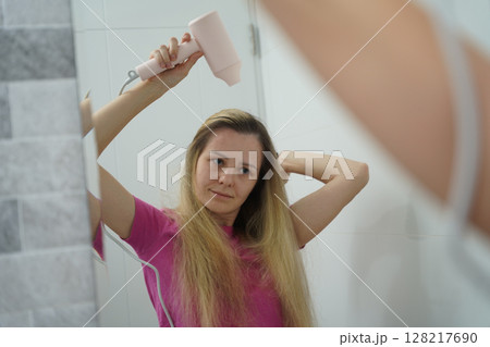 A woman is expertly styling her hair using a blow dryer and brush while in the bathroom 128217690