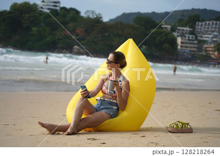 A young woman on the beach lounging on a yellow bean bag A young woman on the beach lounging on a yellow bean bag 128218264
